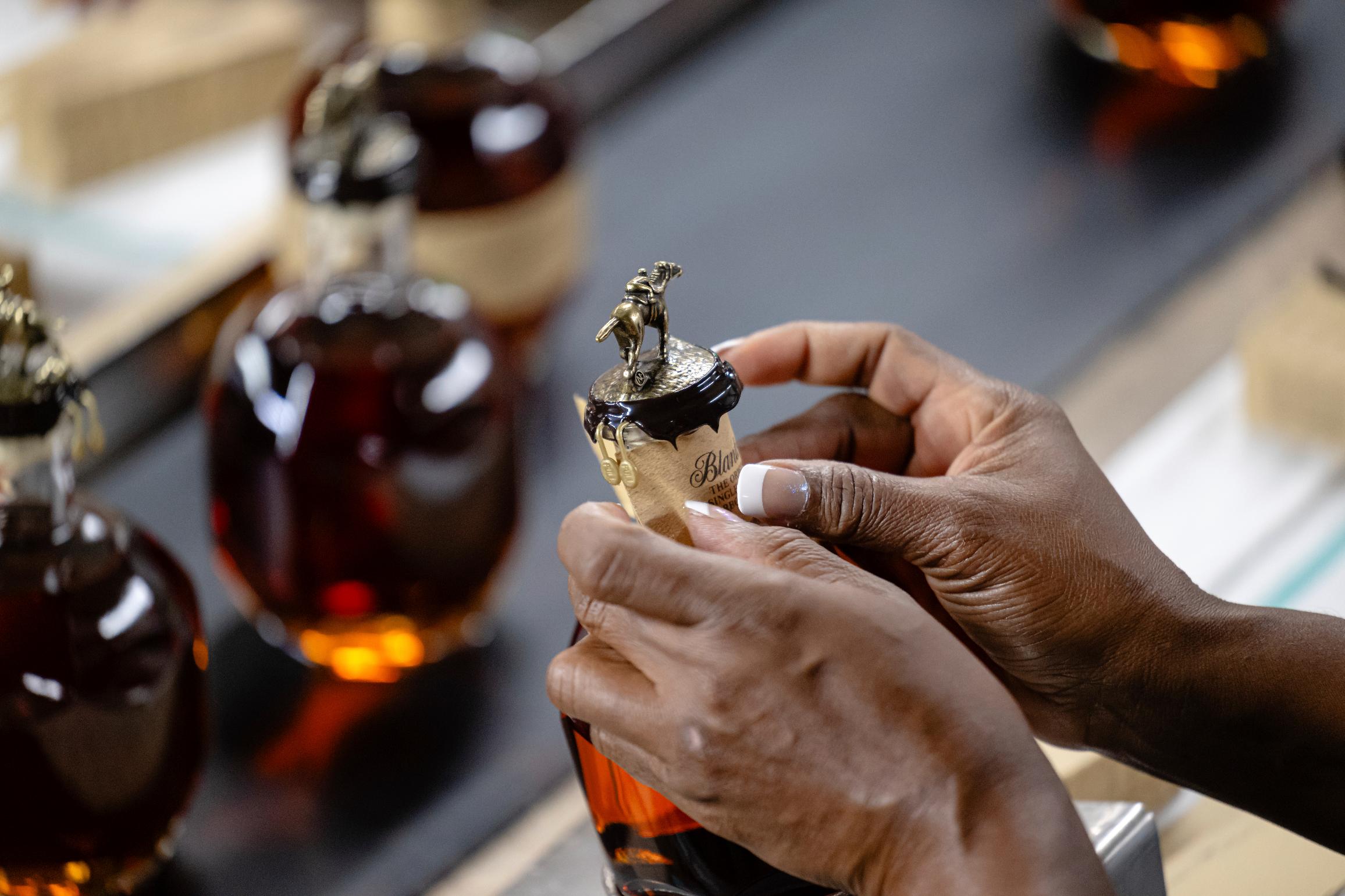 A worker places part of an ornate seal on a bottle of Blanton's bourbon in a bottling area at Buffalo Trace Distillery on Sept. 16, 2025, in Frankfort, Ky. (AP Photo/Jon Cherry)