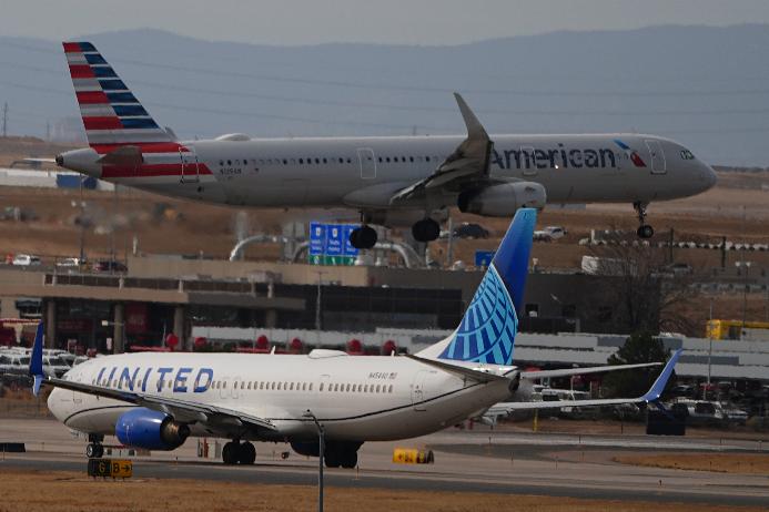 An American Airlines jetliner lands on a runway as a United Airlines plane waits for clearance to take off as high winds strafe Denver International Airport Thursday, March 12, 2026, in Denver. (AP Photo/David Zalubowski)