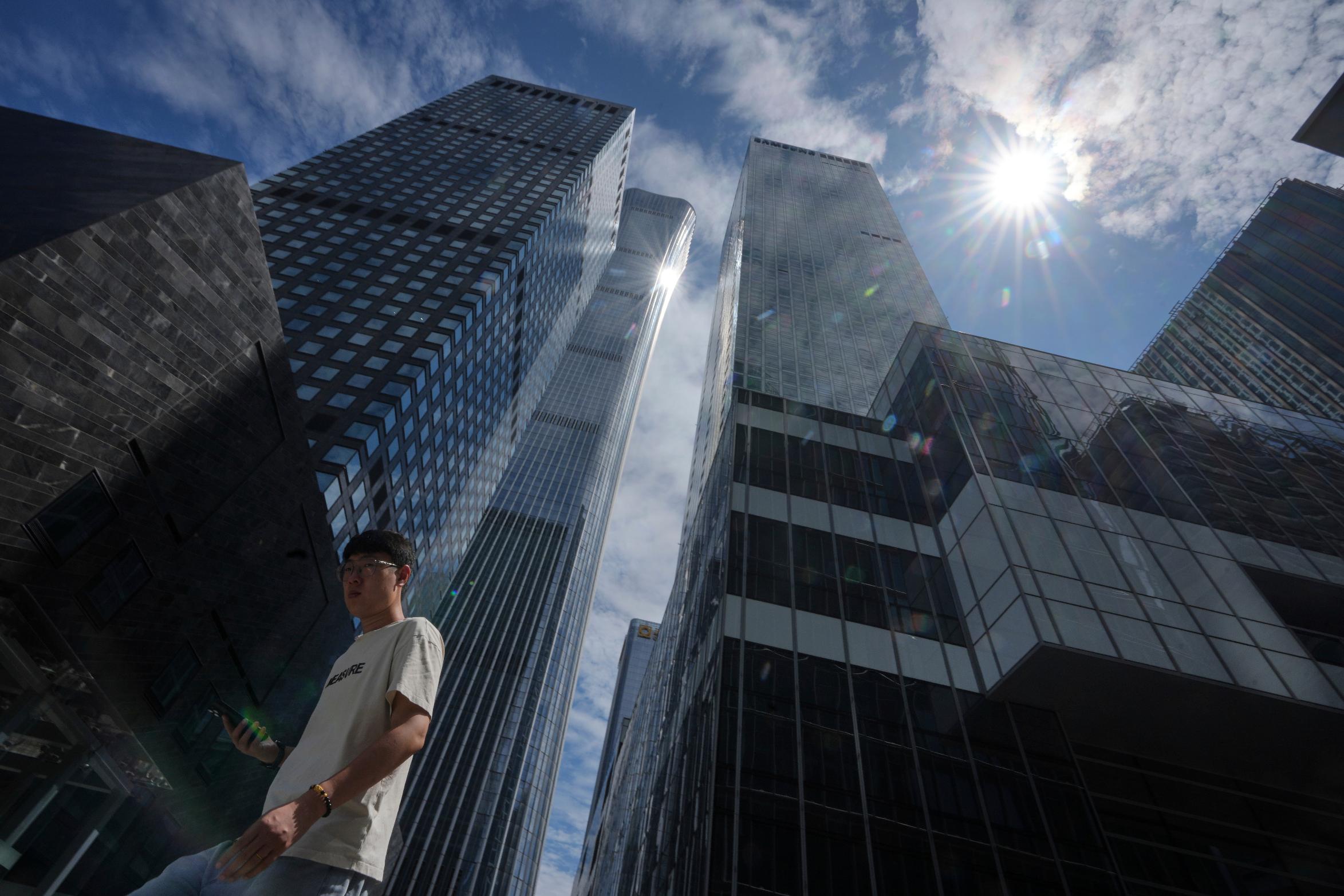 A man walks by the capital city tallest skyscraper China Zun Tower and office buildings at the central business district during lunch break hour in Beijing,, Thursday, Aug. 7, 2025. (AP Photo/Andy Wong)