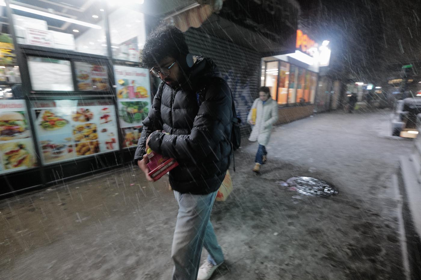 A man carries groceries as snow falls in the Alphabet City neighborhood of New York, Sunday evening, Feb. 22, 2026. (AP Photo/Patrick Sison)