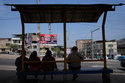 FILE - People sit in a bus station across the street from election campaign signs for presidential and congressional candidates, before the weekend's election in Lima, Peru, Friday, April 10, 2026. (AP Photo/Martin Mejia)