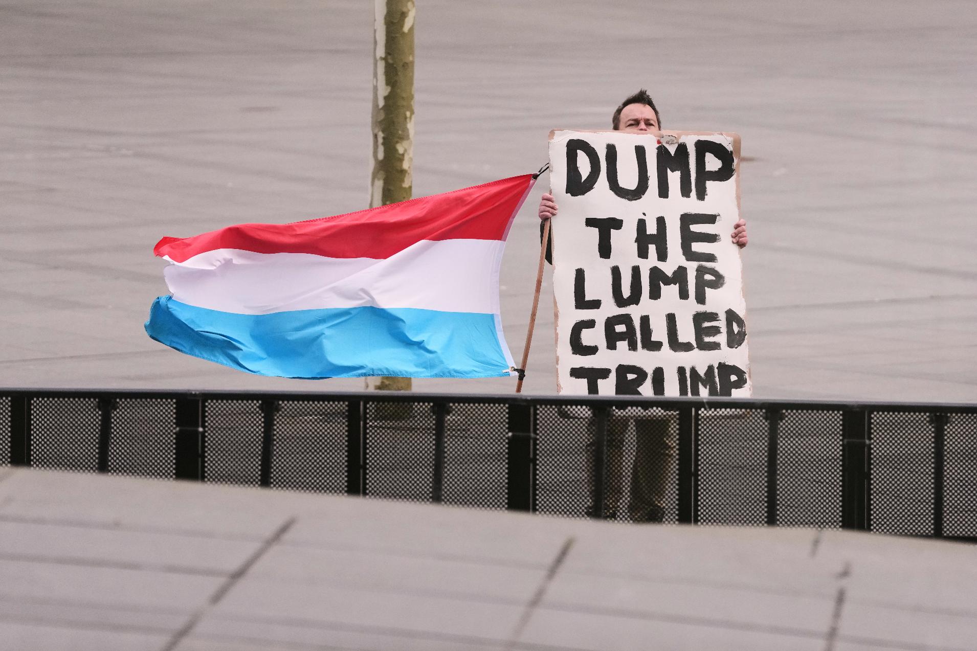 A man holds the flag of Luxembourg and a placard as he demonstrates outside a meeting of EU foreign ministers at the European Council building in Luxembourg, Tuesday, April 21, 2026. (AP Photo/Virginia Mayo)